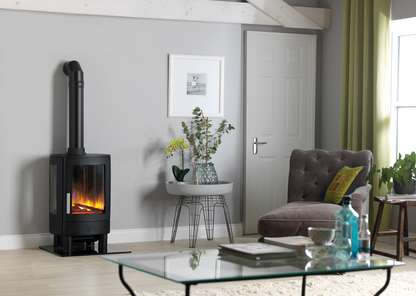 A black wood-burning stove with a visible fire, set in a modern living room next to a gray armchair, glass coffee table, and green curtains.