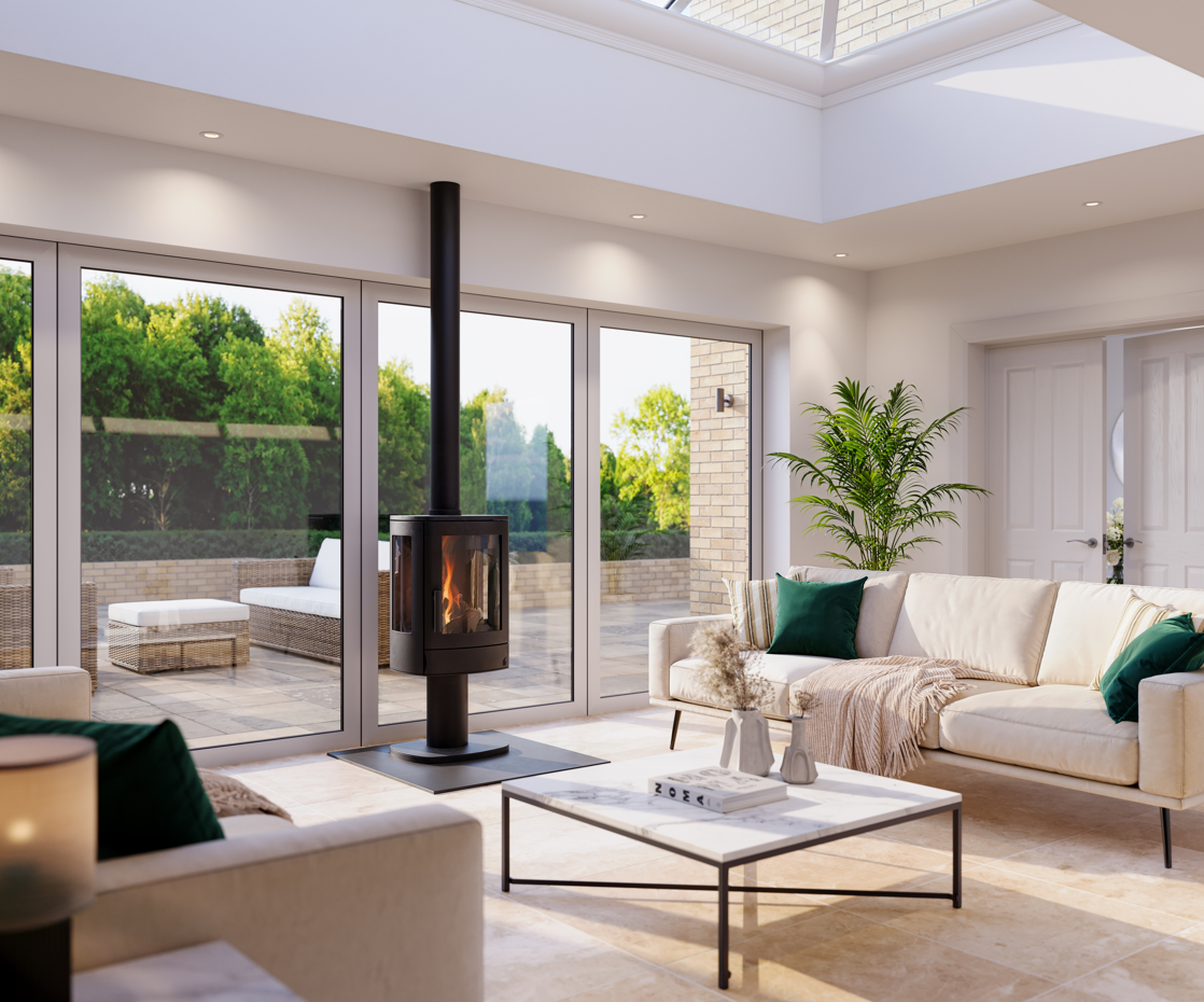 A modern living room with a black wood-burning stove on a slate base, large floor-to-ceiling windows overlooking a garden patio, a cream sofa with green pillows, and a white coffee table.