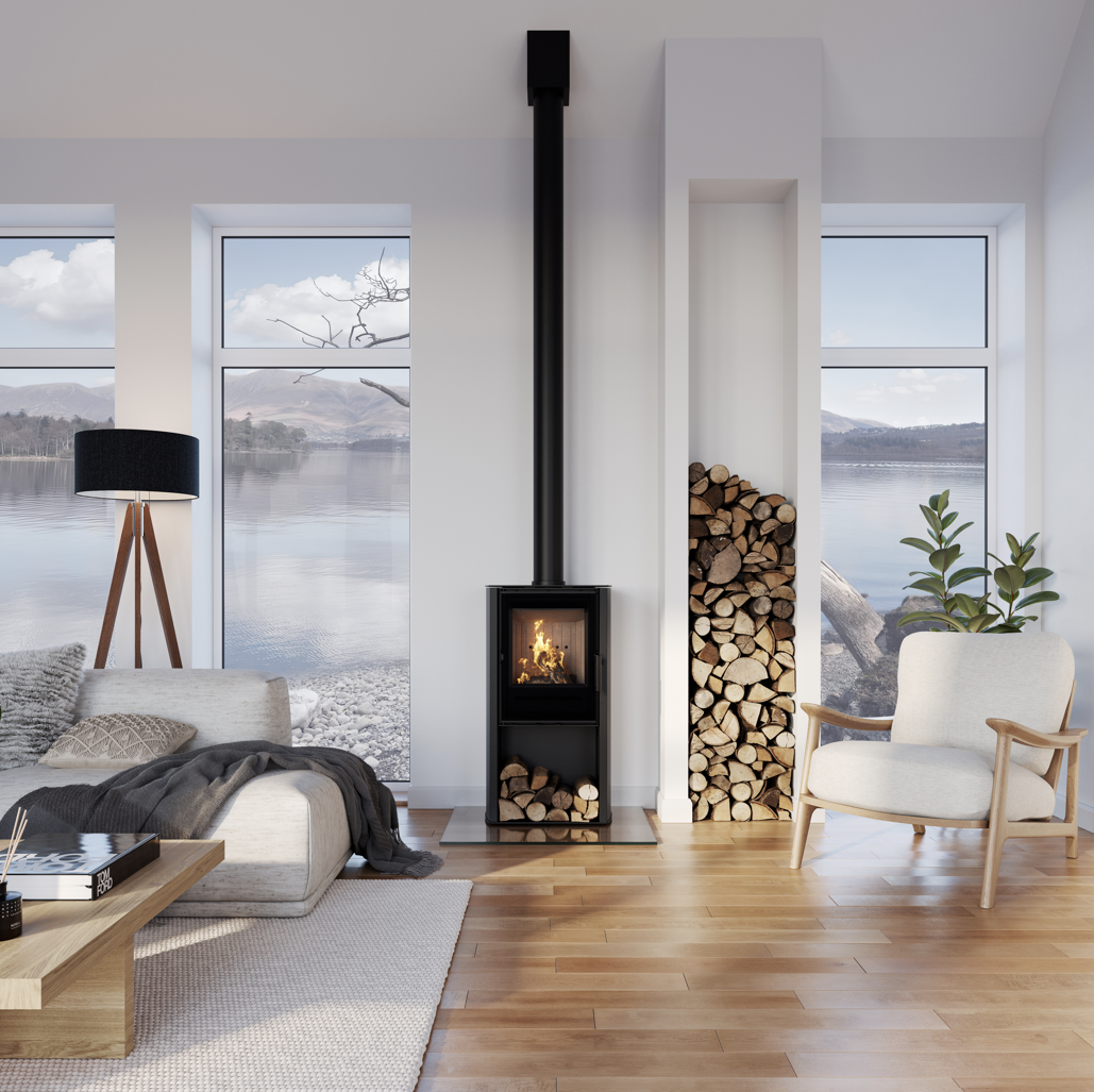 ACR Osprey 5kW. A modern black wood-burning stove with a tall chimney pipe stands in a bright, contemporary living room with hardwood floors, a sofa, and a chair, with a stack of firewood beside it.