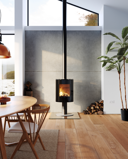 ACR Osprey eVe Pedestal. A modern black wood-burning stove with a visible fire, set in a contemporary room with light wood floors, a concrete wall, and a potted plant.