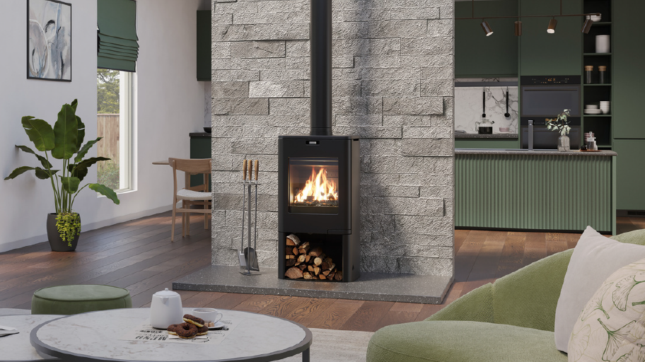A black wood-burning stove with a visible fire, set against a gray stone wall in a modern living room with green furniture and a round coffee table in the foreground.
