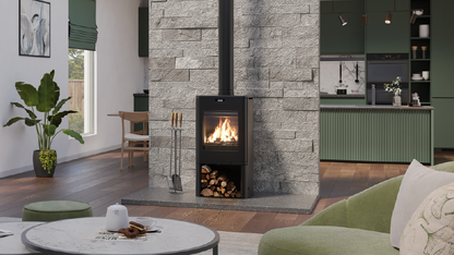 A black wood-burning stove with a visible fire, set against a gray stone wall in a modern living room with green furniture and a round coffee table in the foreground.