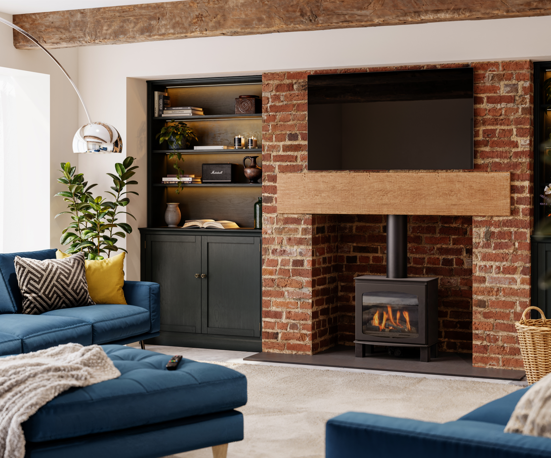 A modern living room featuring a black wood-burning stove insert set into a red brick fireplace with a light wood mantel. The room includes a blue sofa, a matching ottoman, a built-in dark cabinet with shelves, and a large floor lamp.