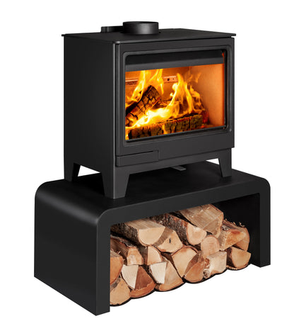 A black wood-burning stove side angle with a glass front door sitting on a bench with logs beneath showing a bright fire and logs, isolated on a white background.