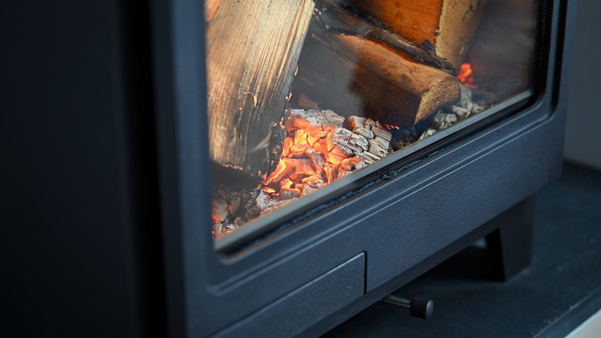 Black wood burning stove with logs and orange embers close up.