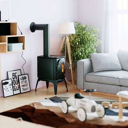 A black metal wood-burning stove with a chimney pipe stands in a modern living room setting next to a gray sofa, a floor lamp, and a potted plant.