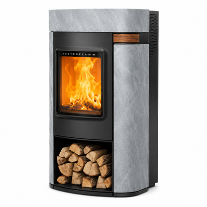 A modern Austroflamm wood-burning fireplace with a black metal frame, a glowing orange fire visible through the glass door, a lower log storage compartment filled with firewood, and a textured gray side panel.