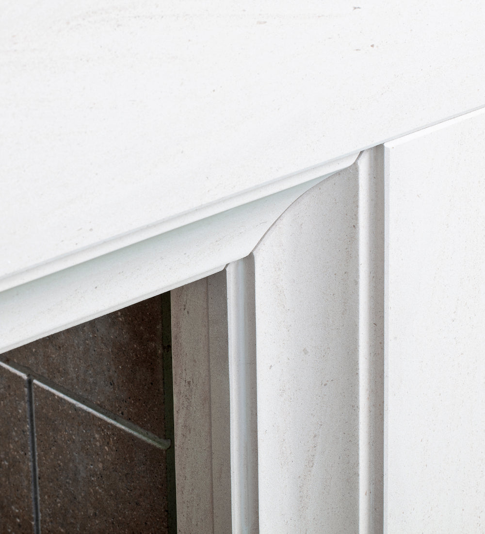 Close-up detail of a white fireplace mantel with a curved inner trim and vertical fluting, set against a dark brown tiled hearth.