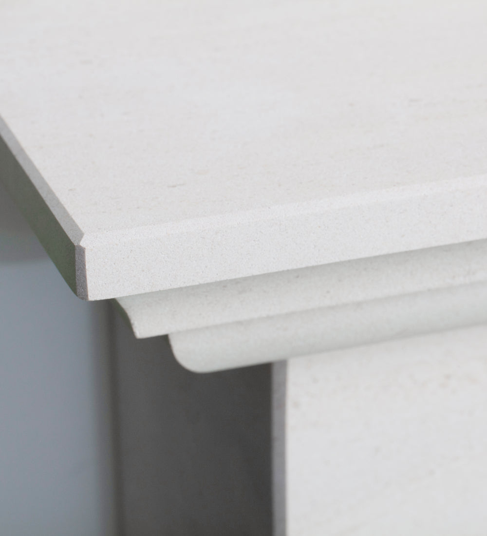 Close-up of a white fireplace corner showing the top edge, front apron, and side profile with a subtle speckled texture.