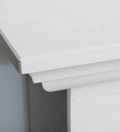 Close-up of a white fireplace corner showing the top edge, front apron, and side profile with a subtle speckled texture.