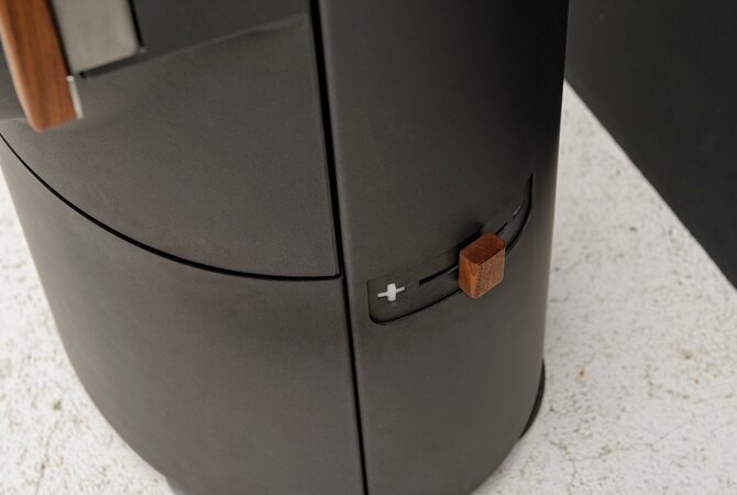 Close-up of a dark gray cylindrical appliance, likely an air fryer, showing a side control dial with a small wooden knob on a light speckled countertop.
