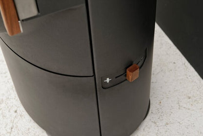 Close-up of a dark gray cylindrical appliance, likely an air fryer, showing a side control dial with a small wooden knob on a light speckled countertop.