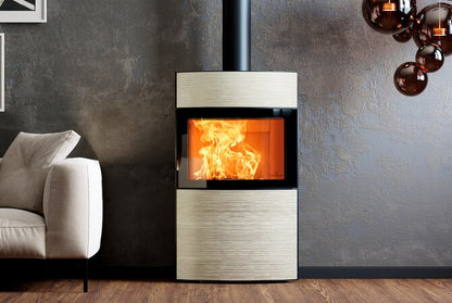 A modern wood-burning fireplace with a black metal frame and a visible orange fire, set against a textured gray wall in a styled interior with part of a light beige armchair and hanging amber glass decor visible.