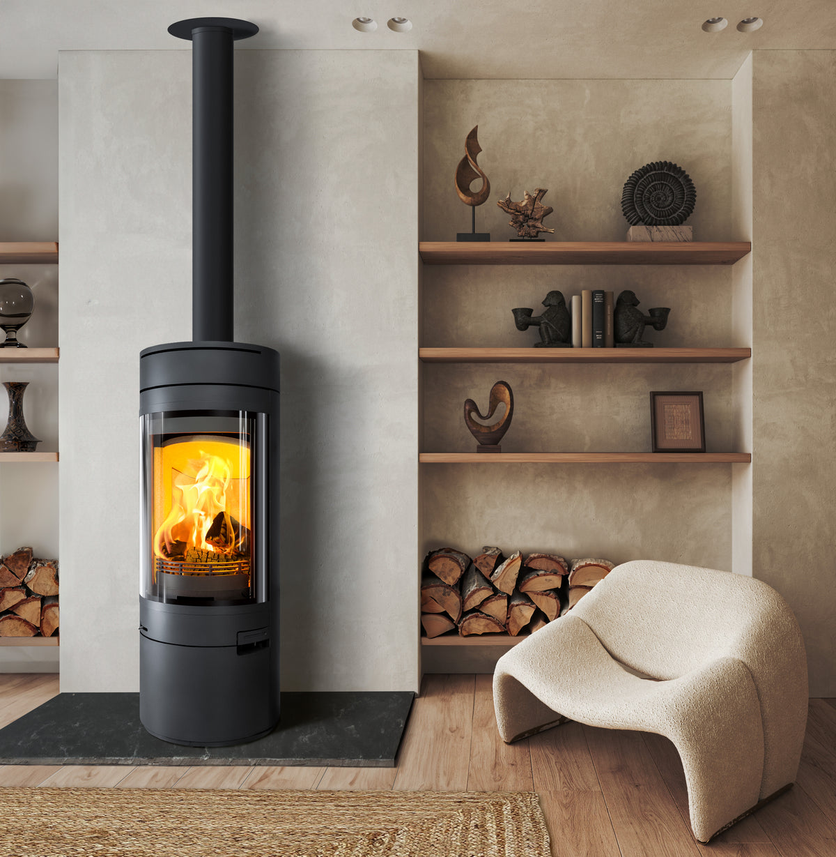 A modern black wood-burning stove with a tall chimney stack, lit with a warm orange fire, set in a styled living room with a curved beige armchair and built-in shelving.