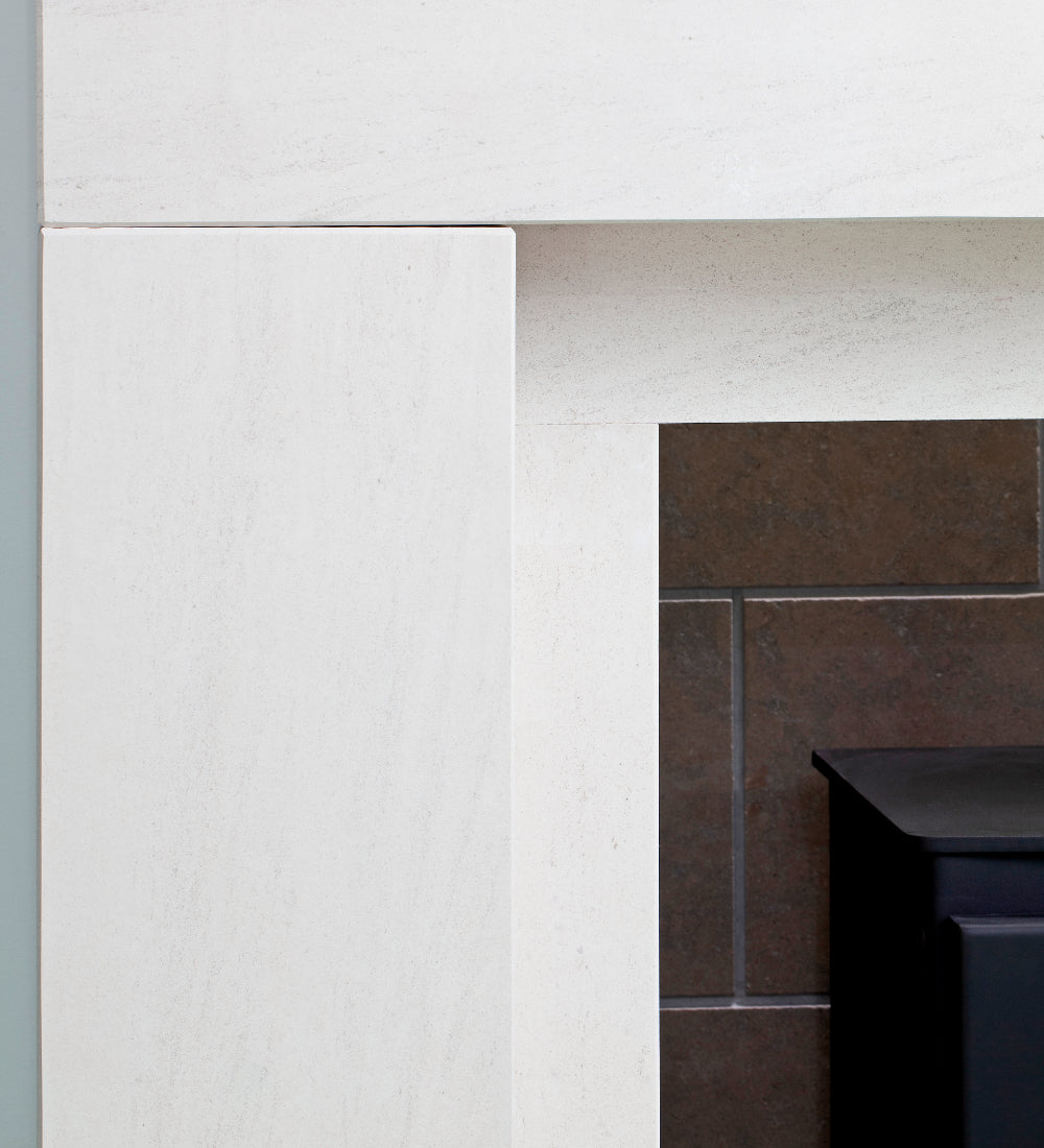 Close-up of a white stone fireplace surround with a dark brown tiled hearth and a black metal firebox insert partially visible on the right.