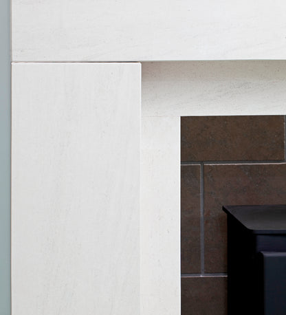 Close-up of a white stone fireplace surround with a dark brown tiled hearth and a black metal firebox insert partially visible on the right.
