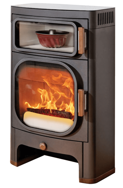 A freestanding wood-burning stove with a dark brown metal body, glass doors, copper-toned handles, and visible flames with glowing embers inside. A small decorative bowl sits in the upper shelf compartment.