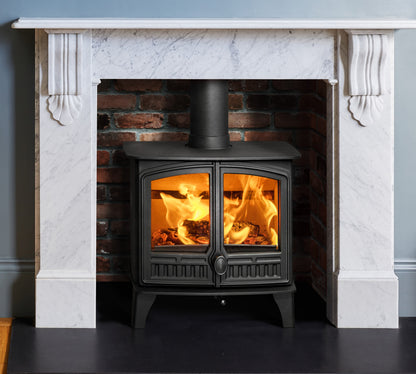 A black wood-burning stove with glowing orange flames, set within a brick fireplace surround framed by a white marble mantel.