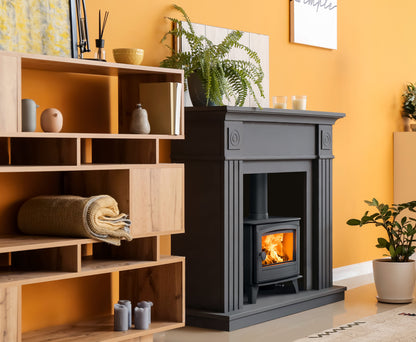A dark gray fireplace insert with a glowing fire, set in a warm yellow-orange room next to wooden shelving.