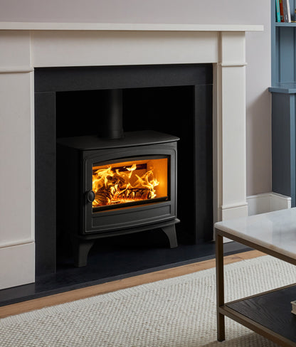 A black wood-burning stove with a glowing orange fire inside, set within a white fireplace mantel in a styled room.