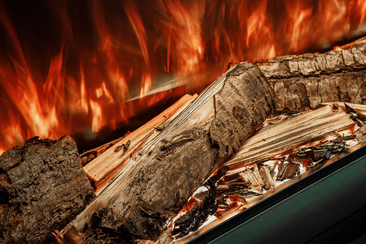 Close-up of a fireplace with burning logs, bright orange and red flames, and charred wood embers inside a dark metal firebox.