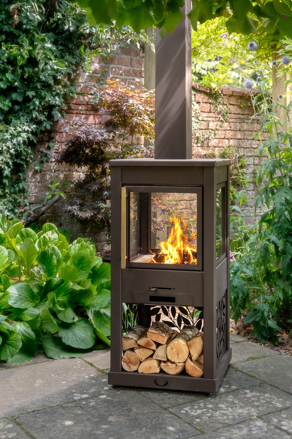 Outdoor patio with a brown metal fire pit, surrounded by shrubs, plants and trees.