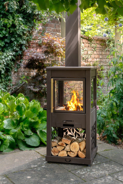 Outdoor patio with a brown metal fire pit, surrounded by shrubs, plants and trees.