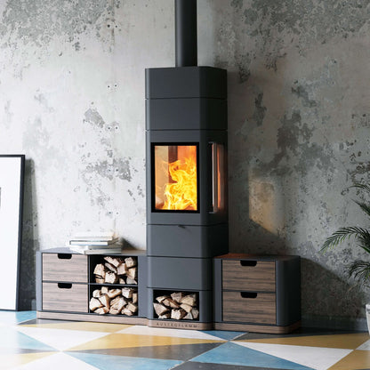 A modern dark gray wood-burning stove with a visible fire, styled in a room with a textured gray wall, geometric patterned floor, and matching wood storage cabinets.