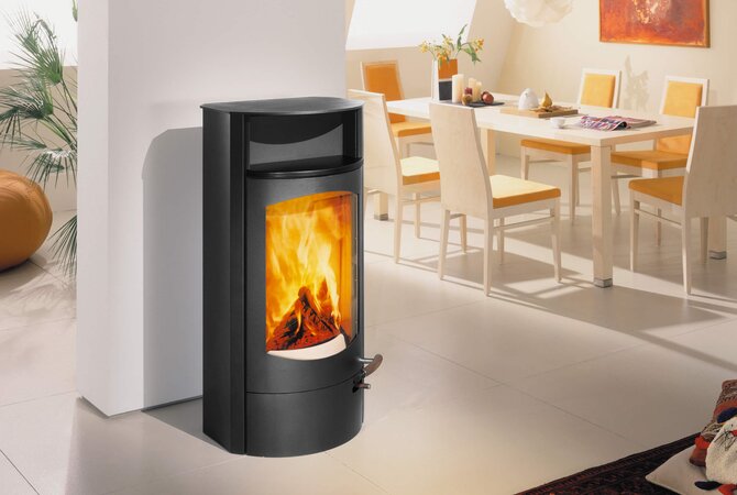 A modern black wood-burning stove with a visible fire inside, positioned in a bright, contemporary dining room setting.