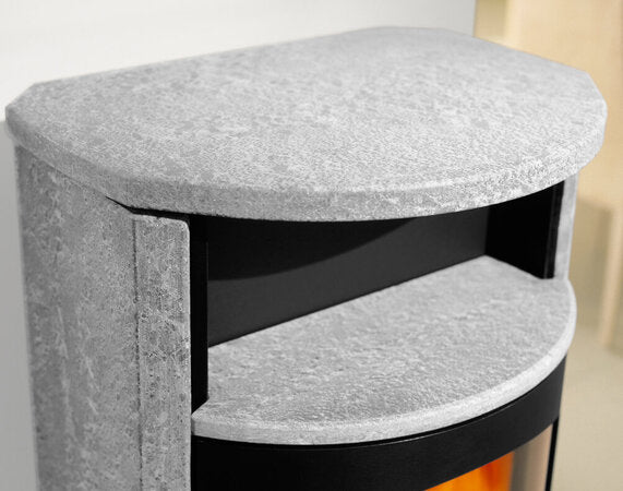 Close-up of a modern fireplace hearth or side table with a light gray felted wool top and shelf, featuring a black firebox insert and a glowing orange fire below.
