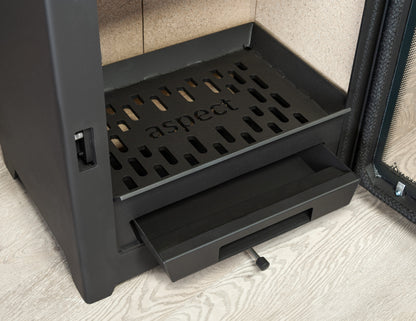 Close-up of a dark charcoal gray Aspect fireplace insert, showing the interior firebox with a perforated grate and a sliding drawer pulled open, set against a light wood floor and textured wall.