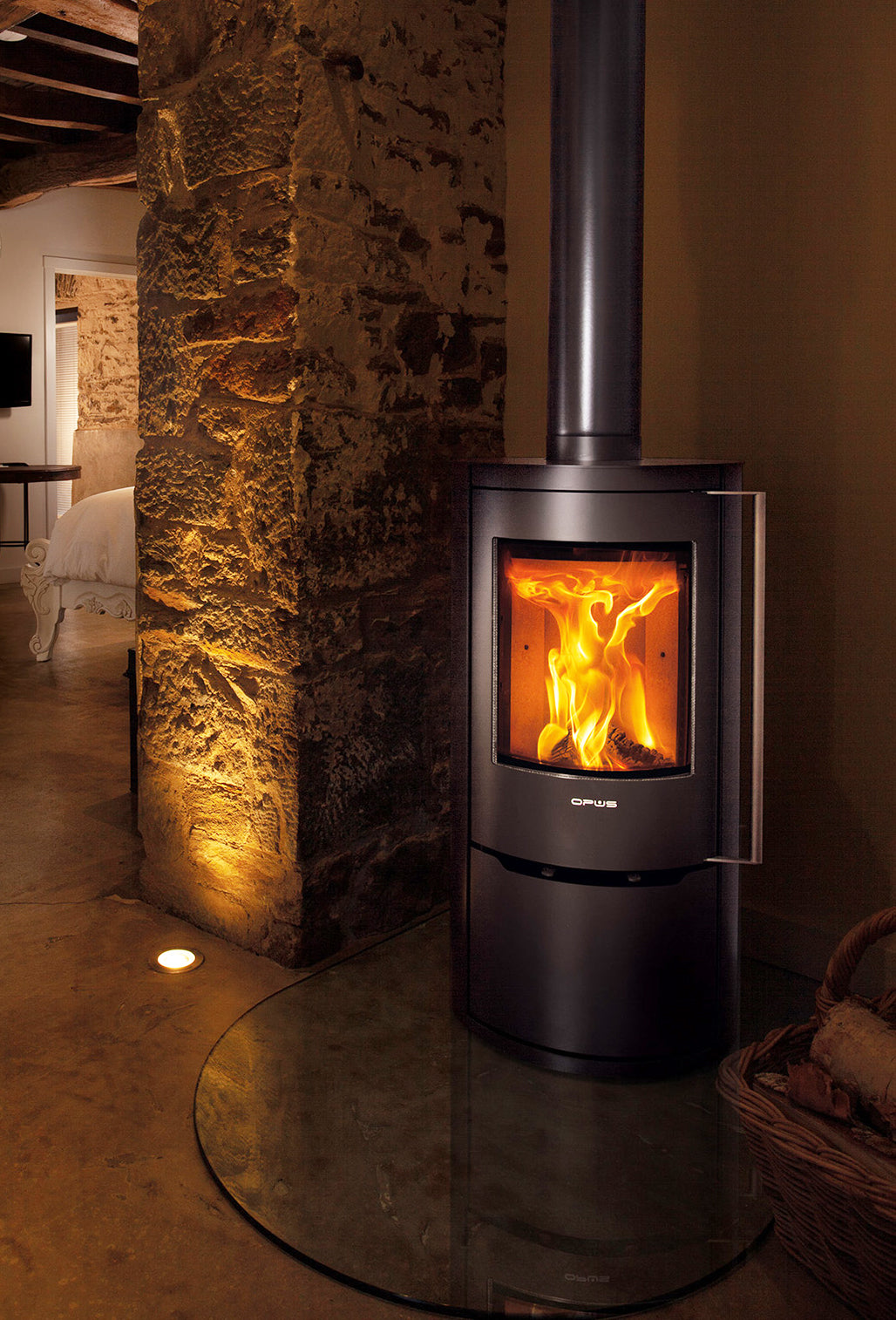 Opus Aria Wood-burning stove with glowing flames inside, set against a stone wall in a cozy room.