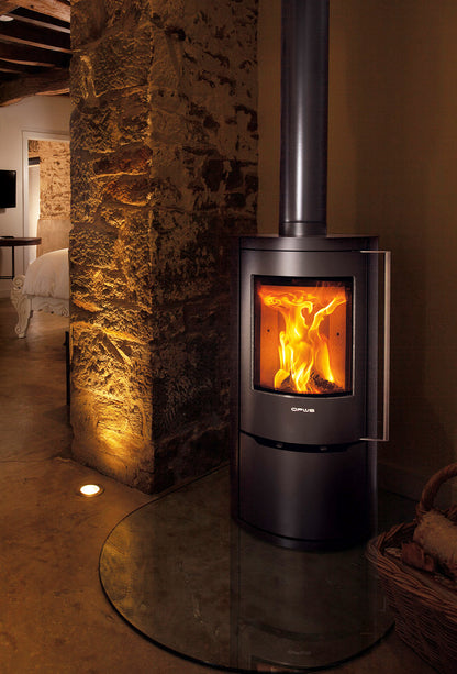 Opus Aria Wood-burning stove with glowing flames inside, set against a stone wall in a cozy room.