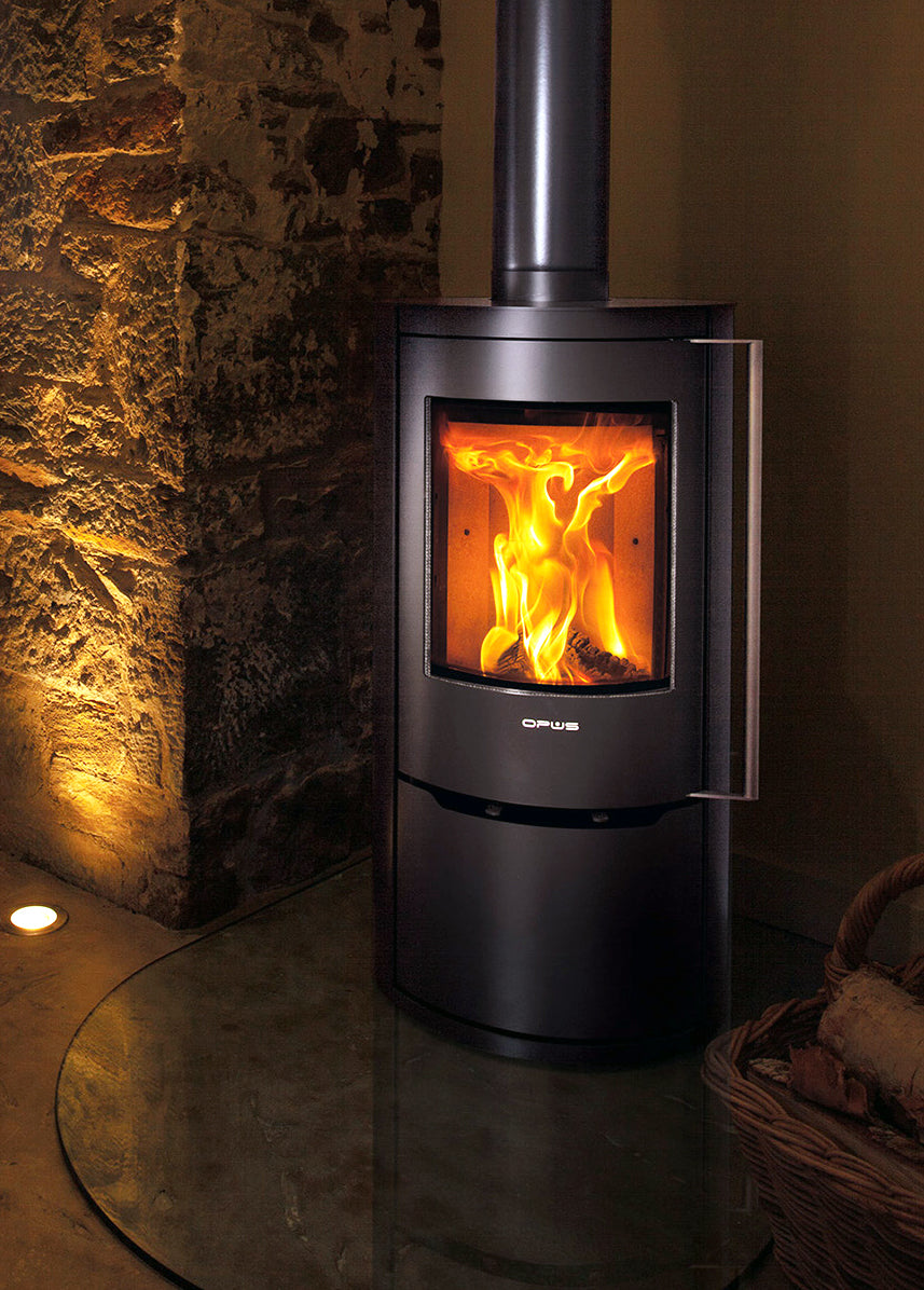 Opus Aria Wood-burning stove with visible flames inside, set against a stone wall.