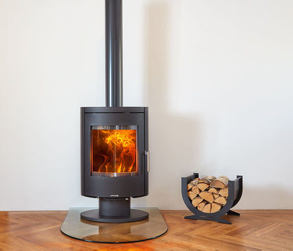 Modern Opus Harmony wood stove with glowing interior on a wooden floor against a white wall