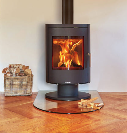 Opus Harmony PR Wood-burning stove showing flames, placed on a glass hearth with wooden floor with a basket of wood logs beside it.