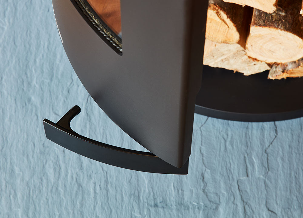 Close-up of a black metal firewood holder against a light blue wall.