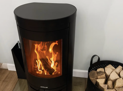 Opus Aria Black wood-burning stove with flames inside, next to a basket of wood on a wooden floor.