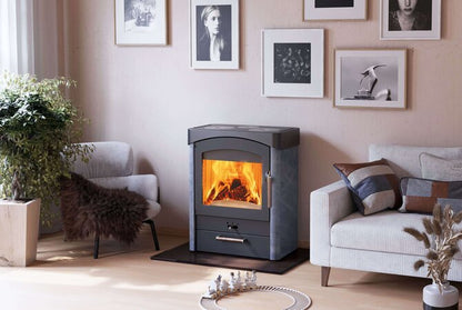 A dark gray wood-burning fireplace with a glowing orange fire inside, set in a cozy living room with a light gray sofa, armchair, and framed wall art.