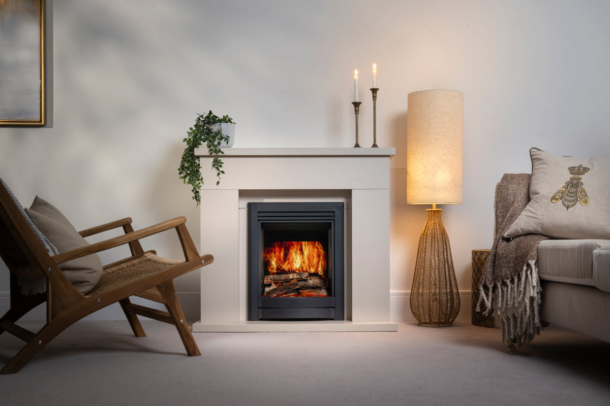 A modern electric fireplace insert with a realistic fire, set in a white mantel within a styled living room featuring a wooden chair, a glowing floor lamp, and a sofa.