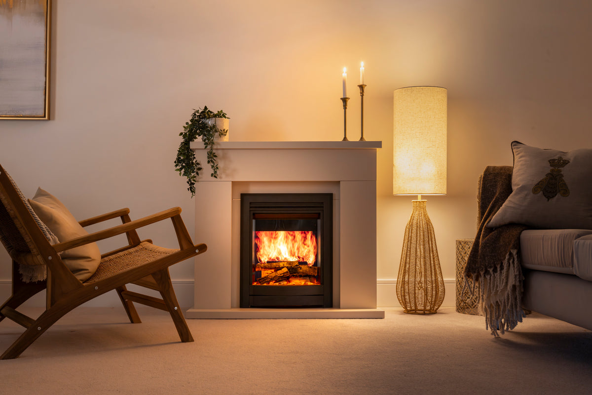 A modern black fireplace insert with a glowing fire, set into a beige wall in a cozy living room with a wooden chair, a floor lamp, and a sofa.