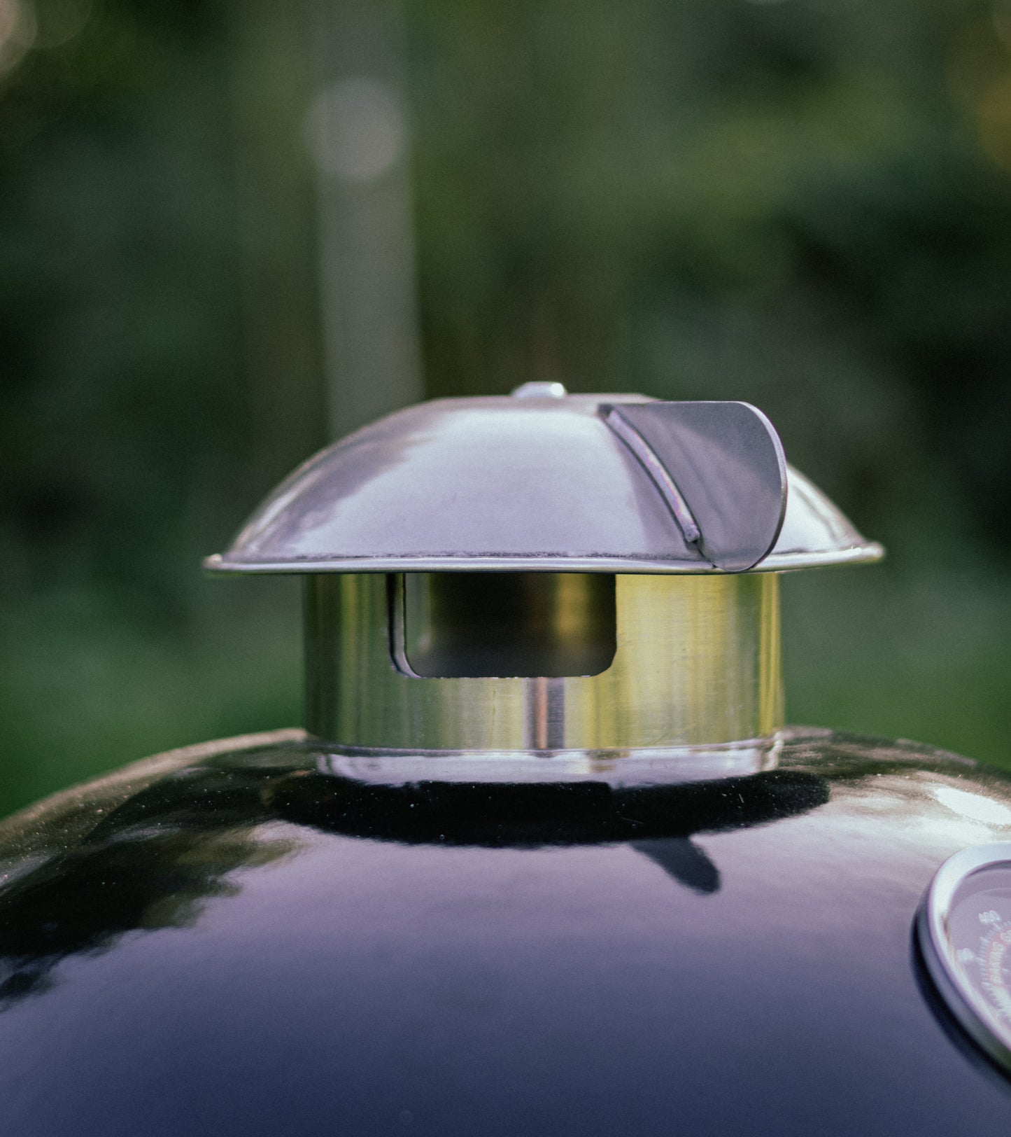 Salamanda Little Cayuga  Metal chimney cap on a grill with a blurred green background