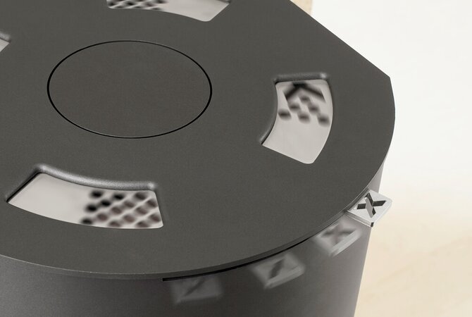 Close-up of a matte black cylindrical stove, showing a circular top panel with cut out details and a small silver accent on the side.