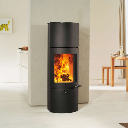 A modern black cylindrical wood-burning stove with a visible orange fire, set against a minimalist beige interior background.