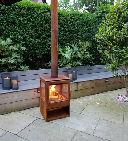 Wood-burning stove in a garden setting with candles and greenery.