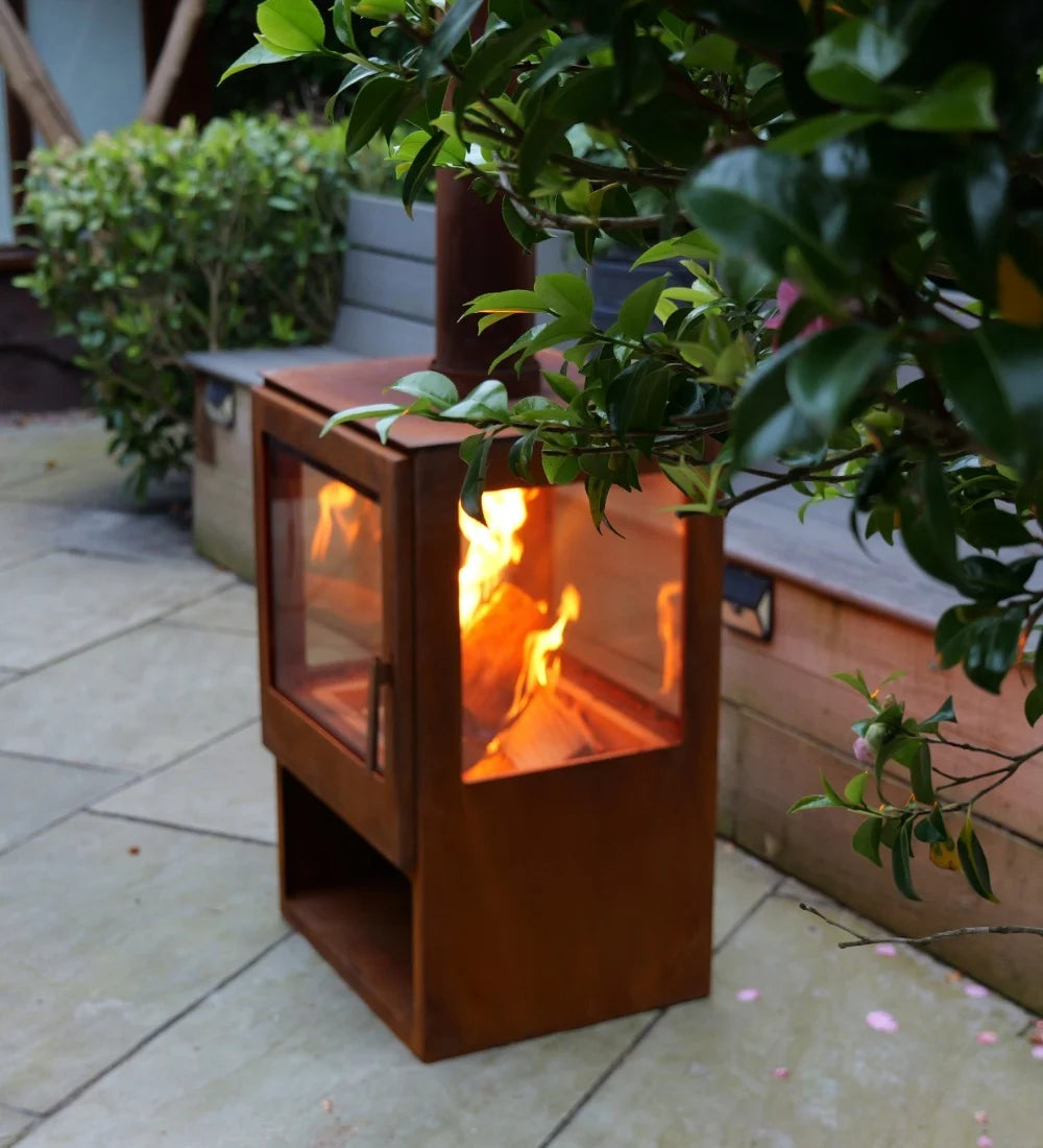 Outdoor fire pit with flames on a patio surrounded by plants
