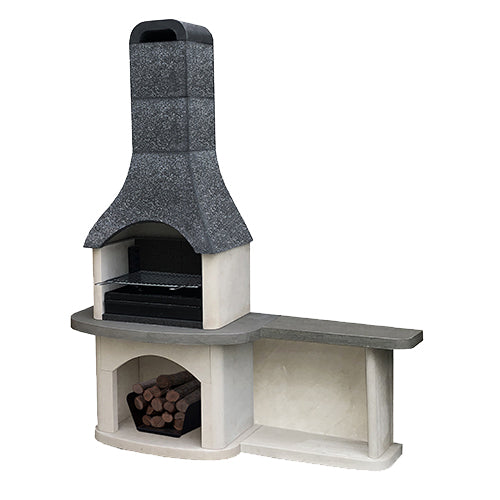 A modern outdoor stone barbecue grill with a chimney stack, set in a lush green backyard patio environment with a wooden dining table and chairs nearby.