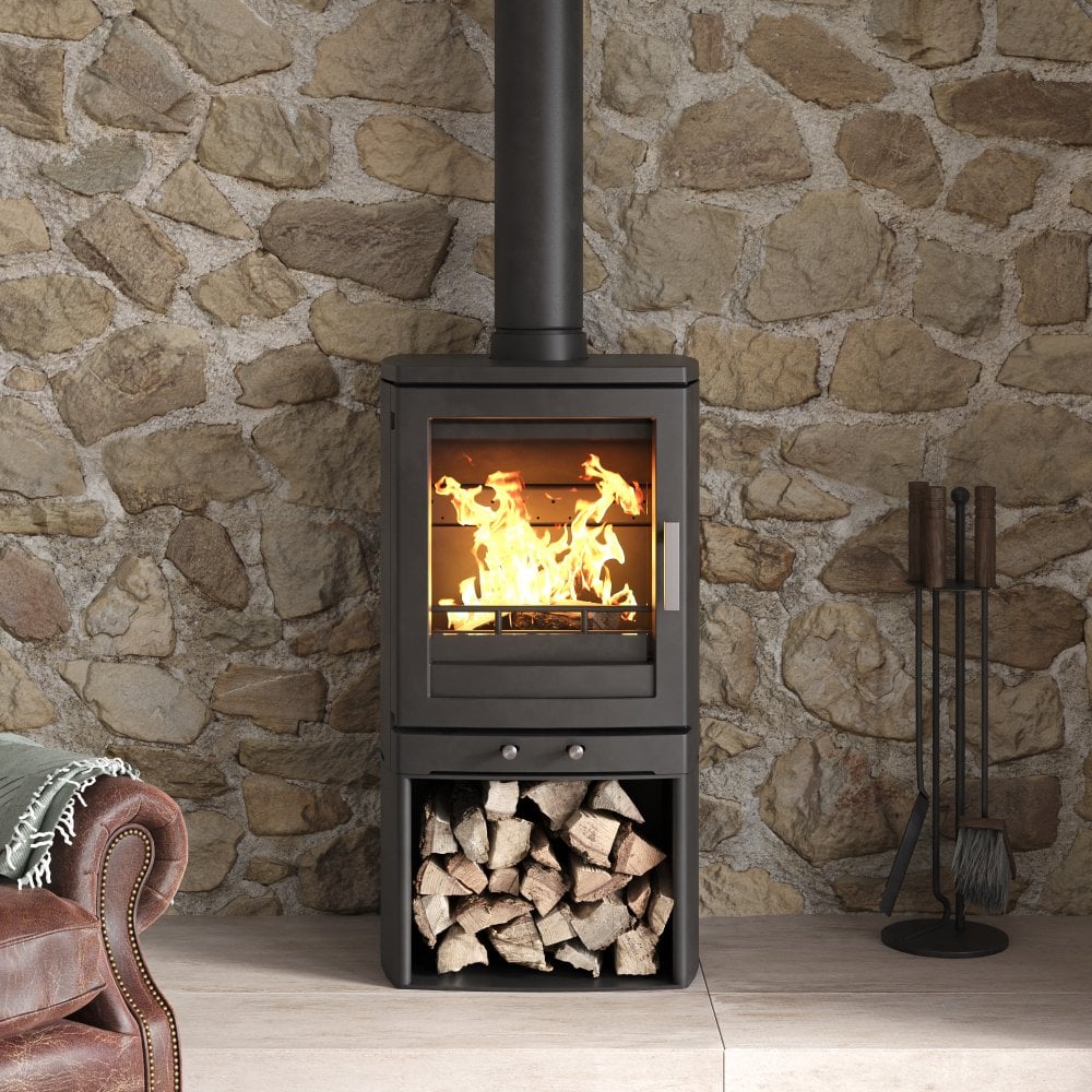 A black wood-burning stove with an open fire visible through a glass door, set against a rustic stone wall. A stack of firewood sits in the lower compartment, and a fireplace tool holder stands to the right.