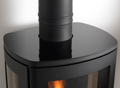 Close-up of a black gas stove with a visible flame inside and a black metal chimney pipe extending upward against a light background.