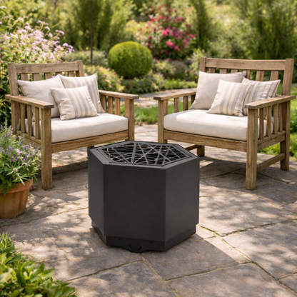 Hexagonal fire pit on a patio with wooden chairs and cushions in a garden setting.